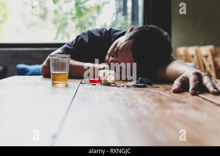 Depressed man with glass of whisky and pills sleeping on table with car keys. Stock Photo