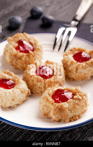 Cookies made from hazelnut shortcake with strawberry jam inside on a white plate with blueberries and a patterned dessert fork on a dark background ne Stock Photo