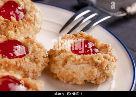 Cookies made from hazelnut shortcake with strawberry jam inside on a white plate with a patterned dessert fork on a dark background nearby. The concep Stock Photo
