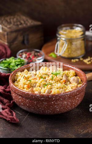 Bulgur with turkey, pork or beef. Eastern dish of rice, delicious traditional food. Stewed meat with grits. Pilaf on dark background Stock Photo