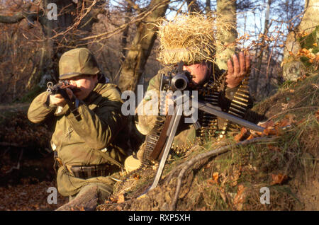 Two WW2 German Reenactor wears the period uniform of a German Waffen SS Soldiers they point an MG42 machine gun and a Kar 98 Rifle. Stock Photo