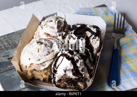 Flat lay of Cinnabons - cinnamon rolls with cream cheese and chocolate, in a paper box, over napkin and wooden blue background. Stock Photo
