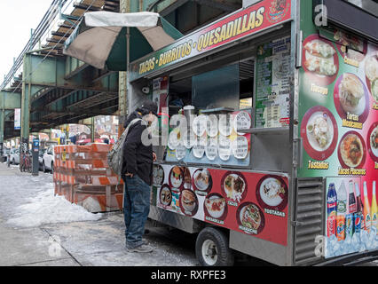 A Latin American worker stops to buy food from a Mexican food cart parked on Roosevelt Ave. under the elevated subway. In Jackson Heights, Queens, NYC Stock Photo