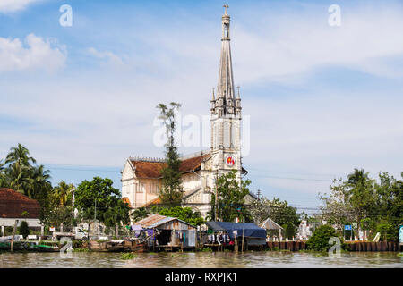 20th century Catholic Cathedral Church behind typical tin shack stilt houses on riverside of Co Chien River in Mekong Delta. Cai Be, Vietnam Stock Photo