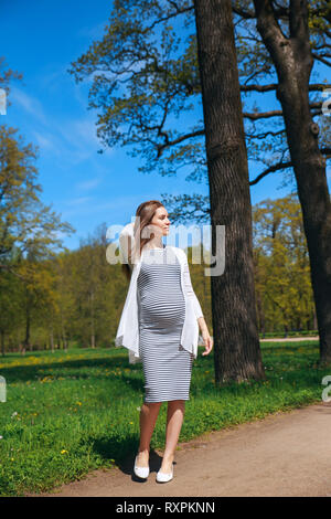 Pregnant woman touching her big belly and walking in the park Stock Photo