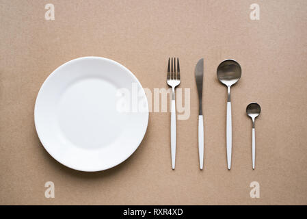 Set of stylish white and chrome cutlery, plate on beige background, top view, copy space. Table setting, menu design. Stock Photo
