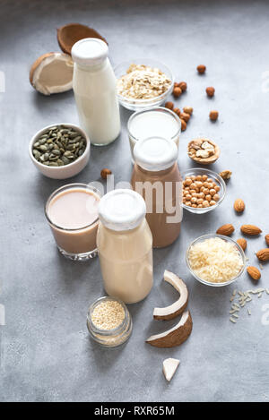 Various vegan plant based milk and ingredients on grey, copy space. Dairy free milk substitute drink, healthy eating. Stock Photo