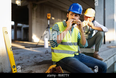 Happy mature and young engineer, architect, worker sitting at building site and resting Stock Photo
