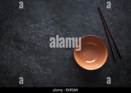 Ceramic bowl and chopsticks on black table, top view, copy space. Empty bowl of Chinese noodles and wooden sticks, asian chinese japanese thai cuisine Stock Photo