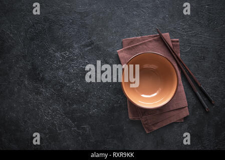 Ceramic bowl and chopsticks on black table, top view, copy space. Empty bowl of Chinese noodles and wooden sticks, asian chinese japanese thai cuisine Stock Photo