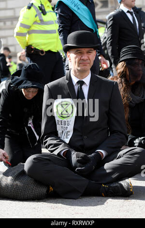 Extinction Rebellion activists are seen blocking the street.  Hundreds of activists from the Extinction Rebellion climate change movement gathered at Parliament Square, marched to Downing Street, and poured 200 litres of fake blood on the ground. This act of non-violent civil disobedience was carried out to demand from the government direct actions to reduce carbon emissions to zero by 2025, speak the truth about climate change and call for a national citizen’s assembly. For the activists, carrying buckets of “blood” to Downing street and spilling it symbolised the violent destiny which faces  Stock Photo