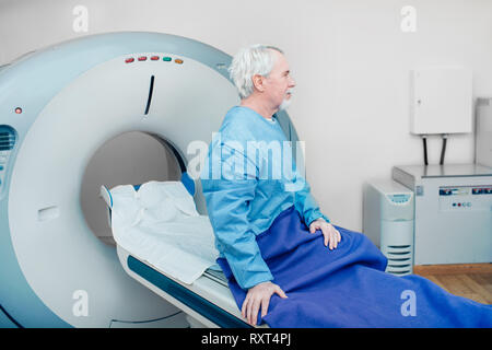 Pensive senior man sitting on scanner table. waiting for CT scan Stock Photo