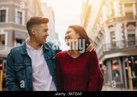 Loving young couple walking on a street looking at each other and smiling. Asian man and woman walking outdoors on city street. Stock Photo