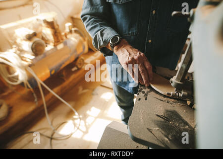 Worker in the carpentry workshop cuts and shapes the wood using band saw. Focus on carpenter hand working in carpentry. Stock Photo