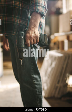 Mid section of carpenter with a hand drill machine at carpentry workshop. Man with drilling machine in hand at workshop. Stock Photo