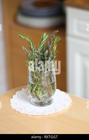 Fresh cut herbs in the kitchen. Thyme and rosemary on the table in a glass of water. Interior of the kitchen, mix of fresh herbs, decoration,  napkin. Stock Photo