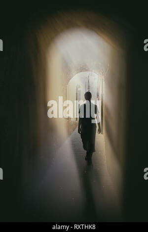 the silhouette of a person in the narrow passage with backlight, vertical mystery wallpaper, book cover Stock Photo