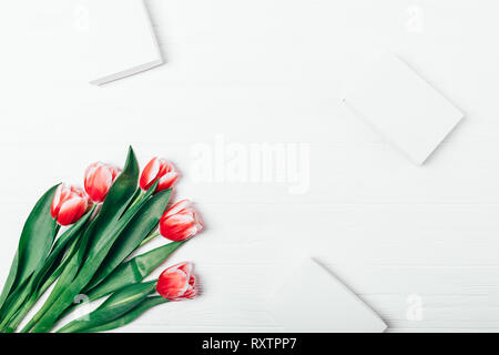 Spring flat lay background of bouquet of red tulips and gift boxes on white wooden table, top view. Stock Photo