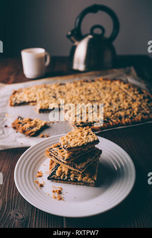 Plate of freshly baked homemade cookies with jam cut into squares near kettle and cup of coffee on brown wooden rustic table. Stock Photo