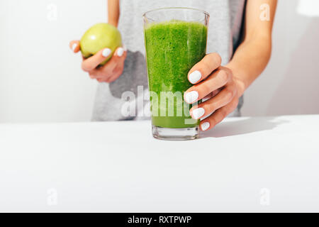 Close-up of woman's hands with manicure holding apple and glass of healthy green smoothie on white background. Stock Photo