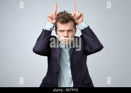 Playful handsome bearded man in suit looking at camera with funny face and horns fingers Stock Photo