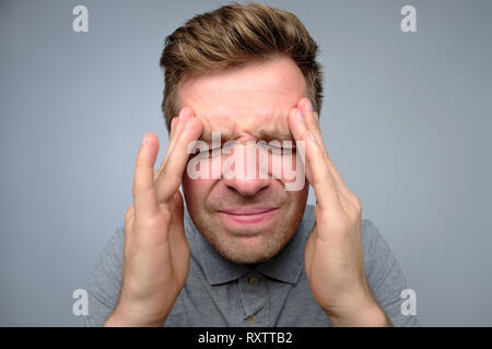Upset unhappy young man squeezing head with hands, suffering from headache. Stock Photo