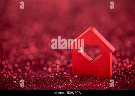 Small house with heart shape on red glitter background Stock Photo