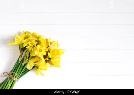Easter greeting card, invitation. Bouquet of yellow daffodils, narcissus flowers lying on white wooden table. Spring concept. Feminine styled stock Stock Photo