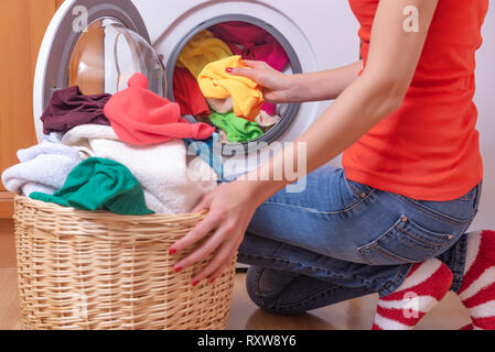 Young woman loads the laundry in the washing machine from the laundry basket before washing. Stock Photo