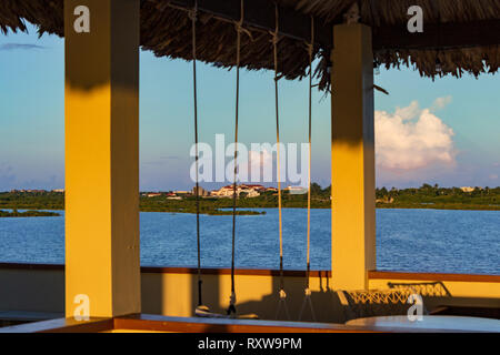 Peering from under a palapa roof toward San Pedro, Ambergris Caye, Belize.  Swings hang from a rafter from which to enjoy the cool sea breeze. Stock Photo