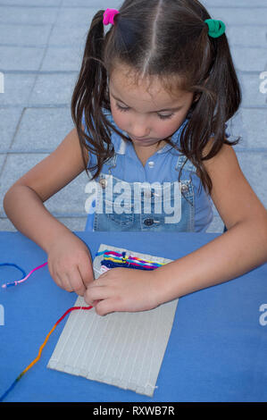 Child girl learning to use cardboard weaving loom. Manual arts workshop for children Stock Photo