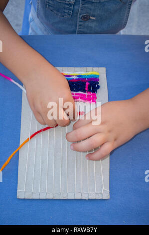 Child girl learning to use cardboard weaving loom. Manual arts workshop for children Stock Photo