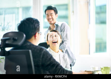 young asian business woman lets out a big laughter while discussing business with two teammates Stock Photo