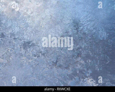 Small circular ice crystals with a light blue color on a frosty window pane, forming a cobblestone pattern. Stock Photo