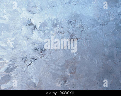 Delicate ice crystals in light and medium blue on a window pane creating an abstract pattern. Stock Photo