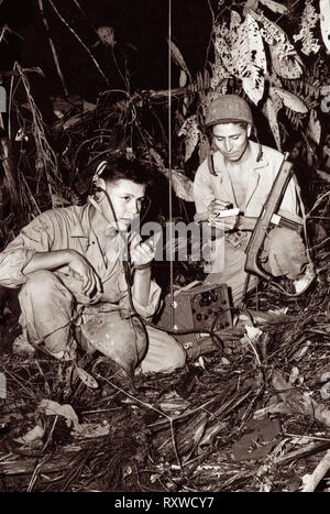 Navajo code-talkers Corporal Henry Bake, Jr., (left) and Private First Class George H. Kirk (right), serving with a Marine Signal Unit, operate a portable radio set in a clearing they've just hacked in the dense jungle close behind the front lines on Bougainville Island in Papua New Guinea during World War II in December 1943. Stock Photo