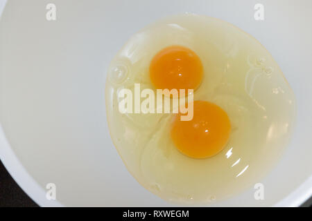 Two broken chicken eggs in a white mixing bowl Stock Photo