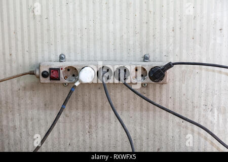 An old electric splitter with sockets and wires with plugs attached to different sides with a broken red switch. Concept of a messy communication syst Stock Photo