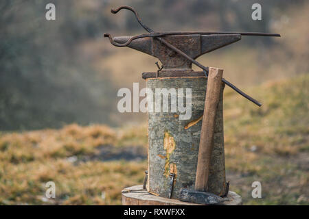 Bolt tongs and a hammer near a old rusty anvil outdoors with blurry background Stock Photo
