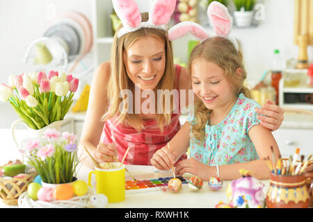 Mother with daughter wearing rabbit ears decorating Easter eggs Stock Photo