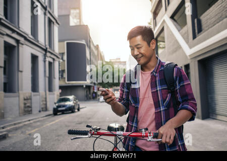 Smiling young man standing with his bike using a cellphone Stock Photo