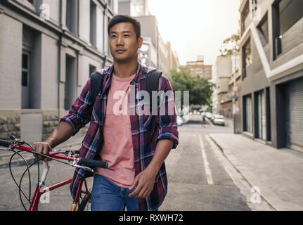 Young Asian man walking with his bike through the city Stock Photo