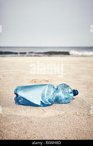 Empty plastic bottle on a beach, selective focus, color toning applied.