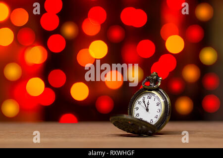 Closeup vintage old clock in the bokeh on brown wood background. The clock is near midnight. Concept Christmas and happy new year or everything relate Stock Photo