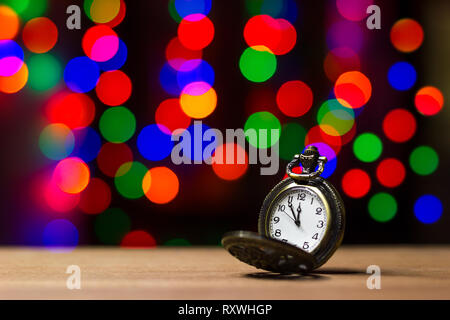 Closeup vintage old clock in the bokeh on brown wood background. The clock is near midnight. Concept Christmas and happy new year or everything relate Stock Photo