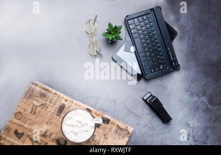office table, coffee, glasses, stapler, cactus, laptop, credit card on concrete table with newspaper Stock Photo