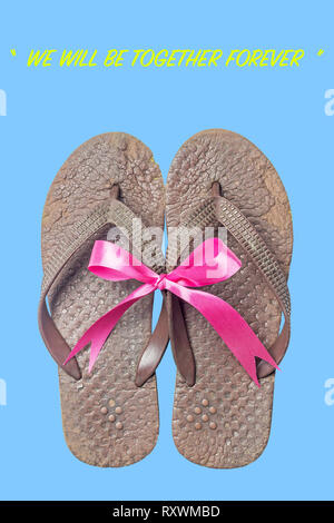 Old sandals on isolate blue background. Brown slippers with pink bow. Concepcion is we will be together forever. Stock Photo