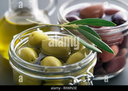 Pickled green and black olives in glass jar with branch leaves close up Stock Photo