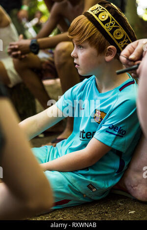 Young boy in an embroidered skull cap at a woodland bushcraft workshop at Into the Wild festival, Kent, UK Stock Photo