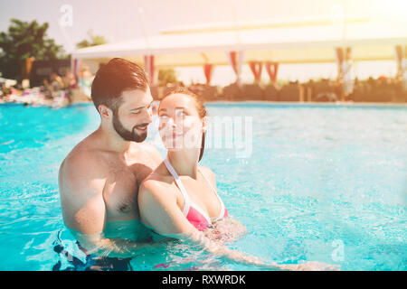 Cheerful youthful guy and lady resting while swimming pool outdoor. Couple in water Stock Photo